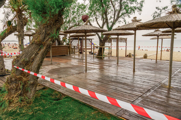 Neoi Epivates, Greece Empty Beach bars prepare to open for summer season. Closed outdoor bar restaurants with bamboo sun umbrellas, no access tape and bathers on sand by the sea.