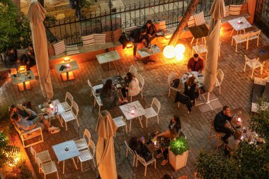 Yunanistan 'da bir bar restoranında gece hayatı sosyal mesafesi. Selanik 'teki boş masaların etrafındaki boş alanların bulunduğu açık alanda mesafelerini koruyan kalabalığa uzun süre maruz kalmak..