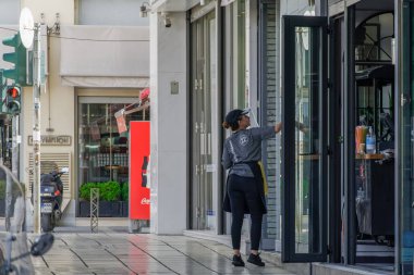 Selanik, Yunanistan barları yaz için ilk gün açılacak. Koruyucu maskeli tezgahtar, Yunan hükümeti COVID-19 Coronavirus tedbirlerini gevşettikten sonra gıda mağazasının girişini temizledi.