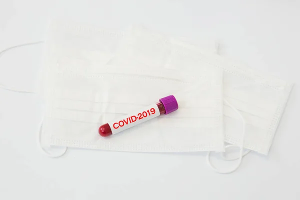 a test tube with a positive result for the COVID-2019 coronavirus test lying on a white medical mask on a white table .