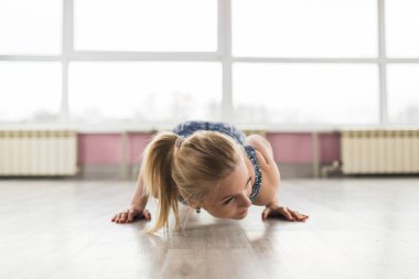 Genç bir Avrupalı kız geniş pencereli parlak bir odada jimnastik yapıyor. Spor salonunda esneme hareketleri. Eğitim ve sağlıklı yaşam tarzı