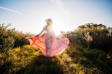 Pembe elbiseli güzel bir kız ve gün batımında yeşil bir tarlada şapkası olan bir kız. Kameraya bak. romantik bahar resmi