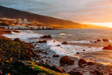 Tropik bir adada, okyanusun üzerinde gün batımı. Şehir dağlarda ve okyanusta gün batımında güneşli bir gecede Tenerife 'de. Pembe okyanus dalgaları. Gradyan ve tahıllı arkaplan rengi, ses efekti. Puerto de la Cruz