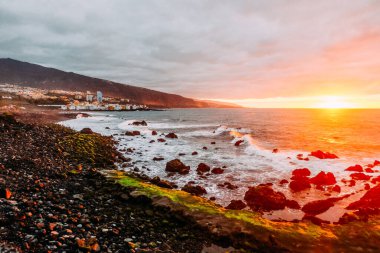 Tropik bir adada, okyanusun üzerinde gün batımı. Şehir dağlarda ve okyanusta gün batımında güneşli bir gecede Tenerife 'de. Pembe okyanus dalgaları. Gradyan ve tahıllı arkaplan rengi, ses efekti. Puerto de la Cruz