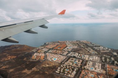 Gökyüzünde uçak kanadı. Deniz kenarındaki şehrin uçak penceresinden bak. Uçakla seyahat kavramı. Gradyan ve tahıllı arkaplan rengi, ses efekti.