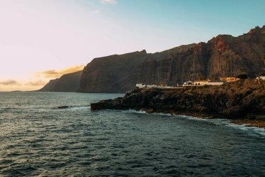 Tropik bir adada, okyanusun üzerinde gün batımı. Şehir dağlarda ve okyanusta gün batımında güneşli bir gecede Tenerife 'de. Pembe okyanus dalgaları. Gradyan ve tahıllı arkaplan rengi, ses efekti. Los Gigantes