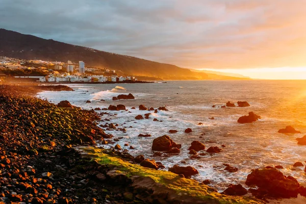 Sunset over the ocean on a tropical island. City in the mountains and ocean at sunset Sunny evening on Tenerife. Pink ocean waves. Background color with gradient and grain, sound effect.  Puerto de la Cruz