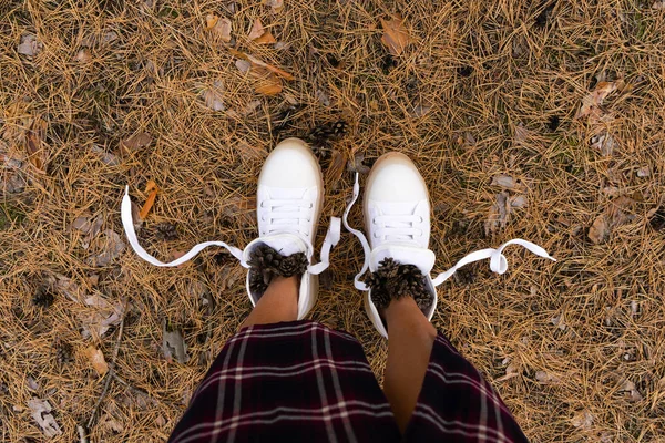 Gambe femminili in stivali bianchi nella foresta con coni. Turismo concetto di turismo. Foresta di conifere. Posa piatta . — Foto Stock