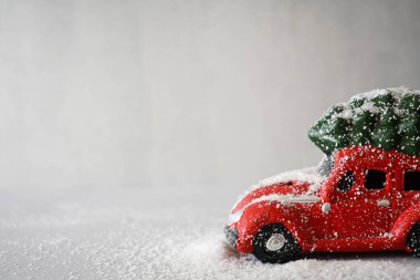 Noel kompozisyonu. Çatıda Noel ağacı olan kırmızı oyuncak araba, gri arka planda. Metin için yer.