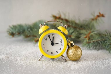 Noel kompozisyonu. Sarı alarm saati ve ladin dallı altın Noel oyuncağı. Gri arka planda kar var..