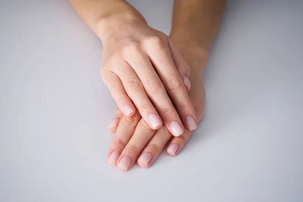 Female hands with a nice manicure on gray background, nude. — Stock Photo, Image