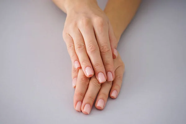 Kobiece dłonie z pięknym manicure na szarym tle. — Zdjęcie stockowe
