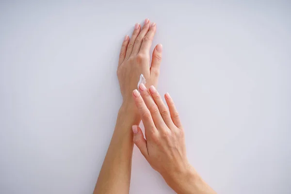 Manos femeninas con crema y una hermosa manicura sobre un fondo gris. Tratamiento de spa . —  Fotos de Stock