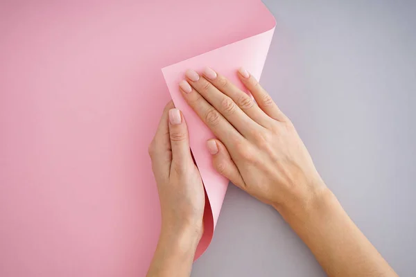 Beautiful hands of a young girl with beautiful manicure on a gray and pink background, flat lay.