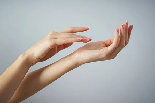 Spa ve Manikür konsepti. Gri bir arka planda güzel manikürlü genç bir kızın güzel elleri.