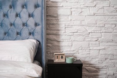 Duvarın yanında yatağı olan güzel bir yatak odası. Komodinin üzerinde bir fincan kahve olan ahşap takvim..