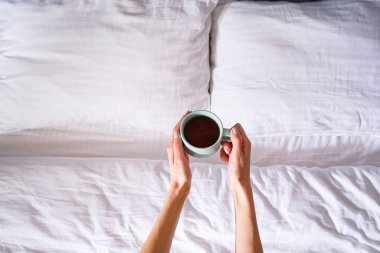 Yatakta elinde bardak tutan genç bir kadının düz elleri vardı. Sabah konsepti.