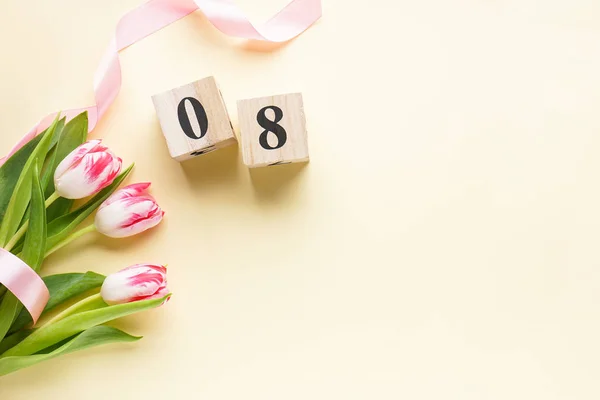 Kadınlar günü, pembe kurdeleli bir buket taze lale ve sarı arka planda ahşap bir takvim. 8 Mart, Uluslararası Kadınlar Günü.