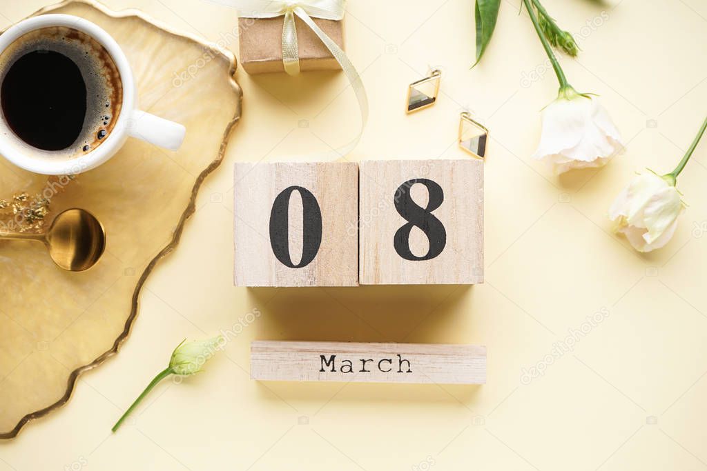 Cup of coffee and a wooden calendar with a gift box, beautiful flowers on a yellow background. Place for text, flat lay