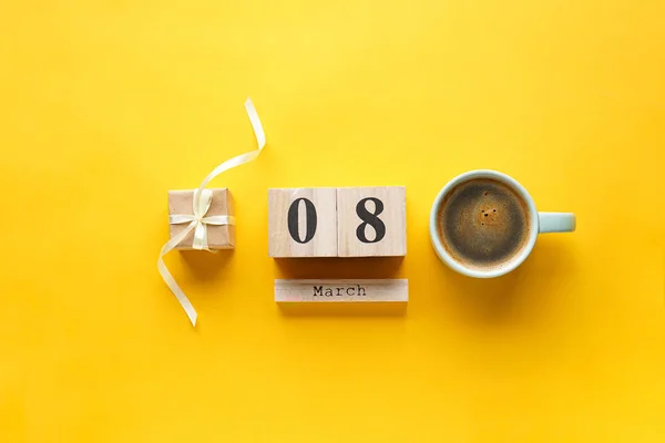 Gift with coffee and March 8 wooden calendar on a yellow background. Flat lay