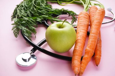 Stetoskop, pembe arka planda elmalı taze havuç. Yakın plan..