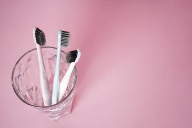 Pembe arka planda bir bardakta diş fırçaları, metin için yeri olan düz bir yer. Diş ve sağlık hizmetleri kavramı.