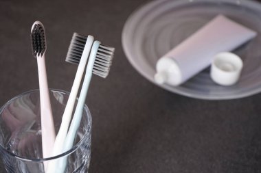 Gri arka planda bir bardakta çok renkli diş fırçaları..