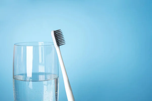 Toothbrush and a glass of water, close-up with space for text on a blue background. Dental and healthcare concept.