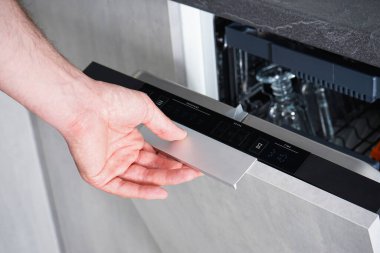 Bulaşık makinesini açıp kapayan bir adam. Bulaşık makinesinde bulaşık yıkıyorum. Adam evi önemsiyor, ödevlerini yapıyor..