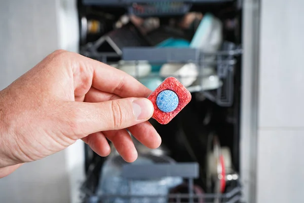 Bulaşık makinesi tableti tutan bir adam. Tabloyu bulaşık makinesine koyuyorum, kapat. Bulaşık makinesi dolu.