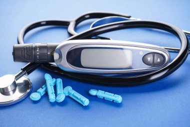 Diyabet konsepti, tıbbi teknoloji. Mavi arkaplanda dijital glukometre ve neşter ve steteskop, yakın plan.. 