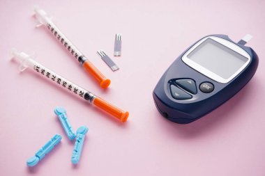 Dijital glukometre ve pembe arka planda şırıngalar. Yakın plan. Diyabet konsepti, tıbbi teknoloji.