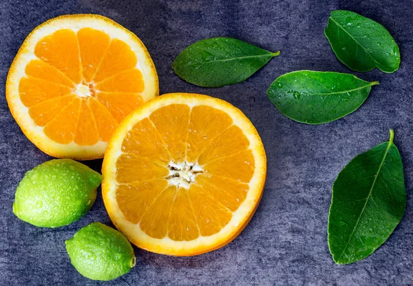 Helle Orangenscheiben, Zitronen und Blätter mit Wassertropfen gegen den dunklen Stein. — Stockfoto