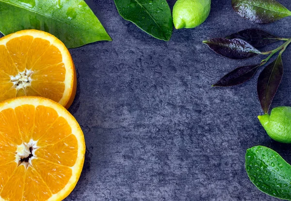 Helle Orangenscheiben, Zitronen und Blätter mit Wassertropfen gegen den dunklen Stein. — Stockfoto