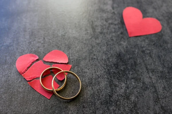 Anéis de casamento e coração vermelho partido. Fundo preto. A concha — Fotografia de Stock