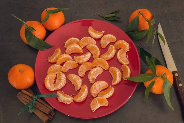 Яркие сочные мандарины лежат на красной тарелке. Коричные палочки — стоковое фото