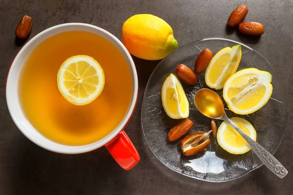 Çay kırmızı bir kupa. Dilim sulu limon, tarihleri ve kaşık bal.