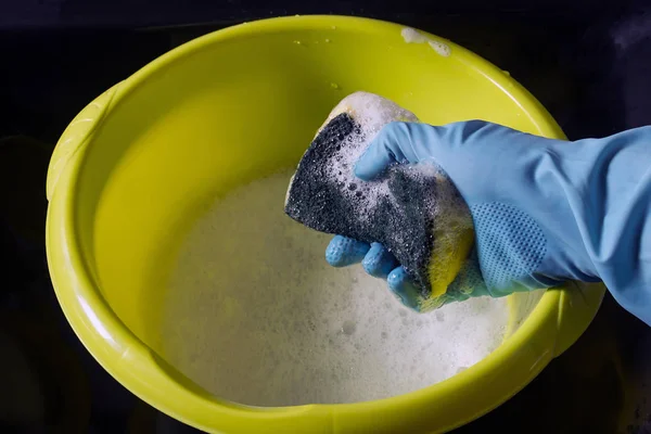 Hand in rubber glove washes sponge in yellow basin. — Stock Photo, Image