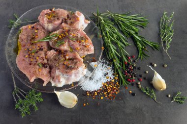 Otlar ve baharatlar ile taze çiğ et karanlık bir yüzeyde taş yatıyor.