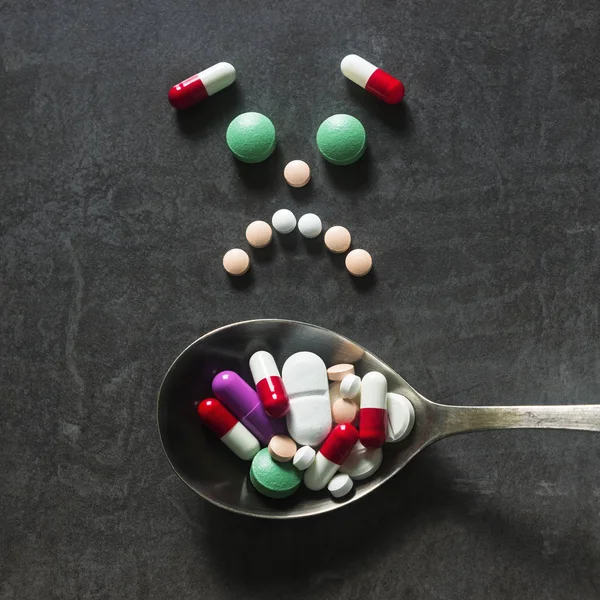 Beaucoup de pilules colorées et onglets avec cuillère sur un fond sombre . — Photo