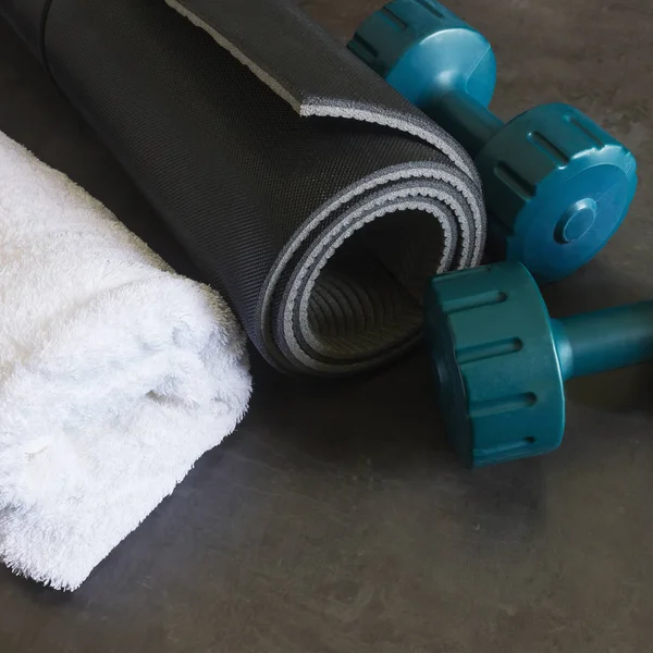 Black yoga mat, two dumbbells and  a white towel lie on a dark stone surface.
