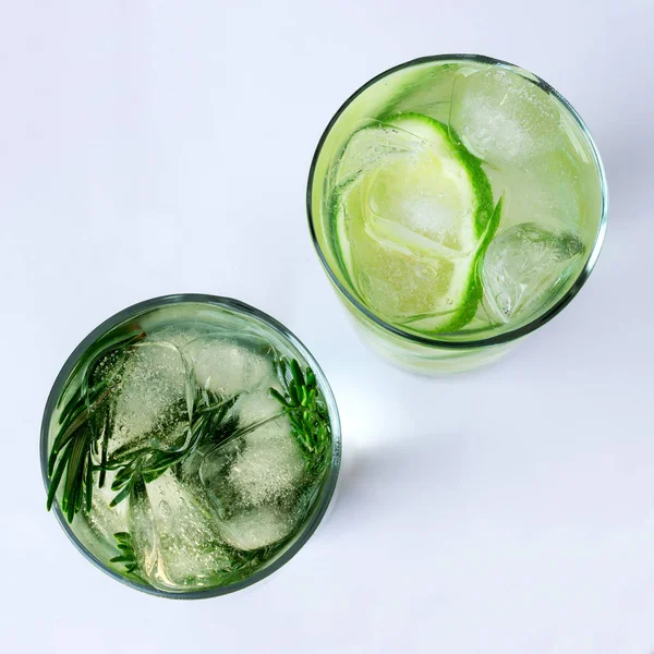 Glass of carbonated drink with lime slices, ice cubes and rosemary twigs on white background.