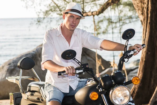 Deniz kenarında bir motosiklet üzerinde oturan yakışıklı adam