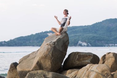genç adam sahilde içinde Thailan bir kayanın üzerinde yoga egzersizleri yapıyor