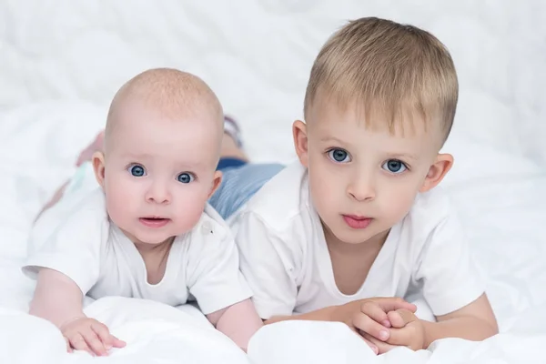 Little kids with blue eyes are lying together on white blanket