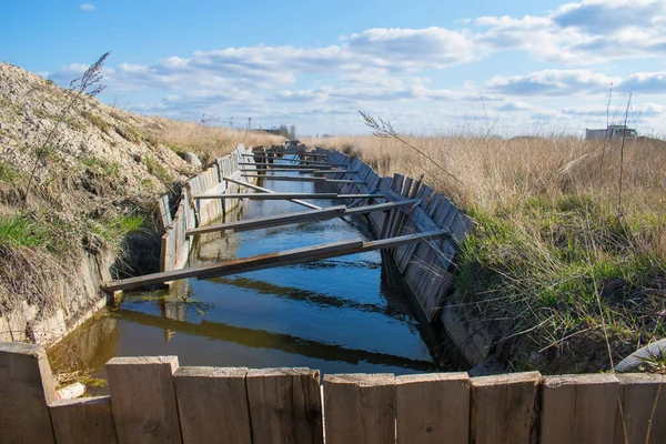 Su hendeği, sulama ve kırsal alanlardaki sulama için ahşap kalaslarla güçlendirilmiş, açık havada bahar öğleden sonra yağmur ve eriyen kar suyuyla dolu.