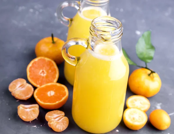 Two bottles of citrus juice served with fresh whole and slice citrus on gray background — Stock Photo, Image