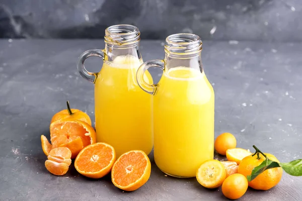 Two bottles of citrus juice served with fresh whole and slice citrus on gray background — Stock Photo, Image