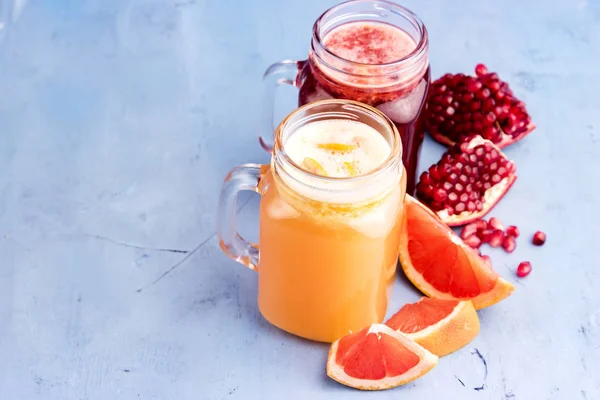 Jars with pomegranate and grapefruit juice on blue background. Refreshments and summer drinks. — Stock Photo, Image