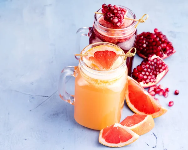 Jars with pomegranate and grapefruit juice on blue background. Refreshments and summer drinks. — Stock Photo, Image